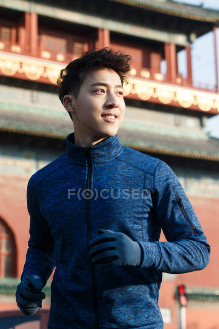 Guapo deportivo joven asiático hombre corriendo y mirando lejos al aire libre - foto de stock