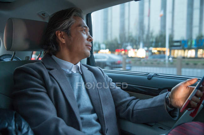 Mature asian businessman sitting in car and using smartphone — Stock Photo