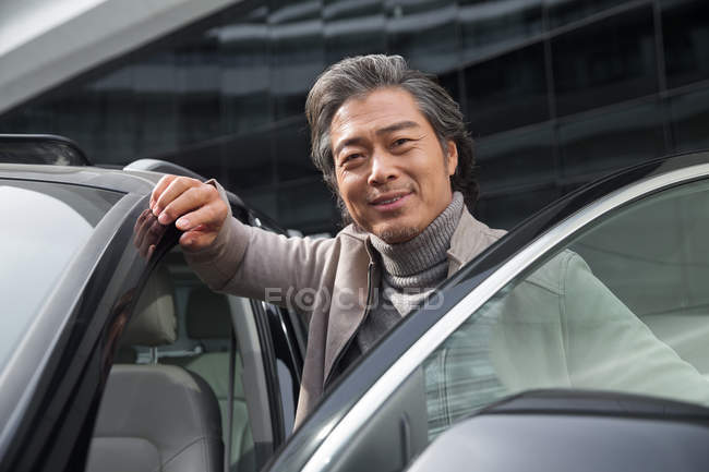 Mature asian man standing near car and smiling at camera — Stock Photo