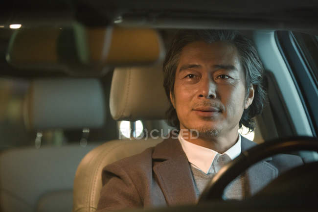Mature asian businessman driving car at night — Stock Photo