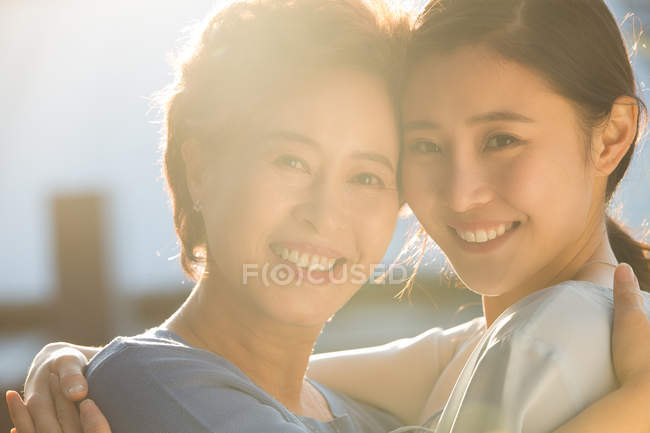 Glückliche Mutter mit erwachsener Tochter, die sich umarmt und im Freien in die Kamera lächelt — Stockfoto