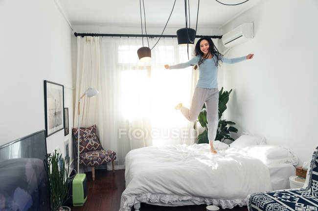 Beautiful happy young asian woman in pajamas jumping on bed — Stock Photo