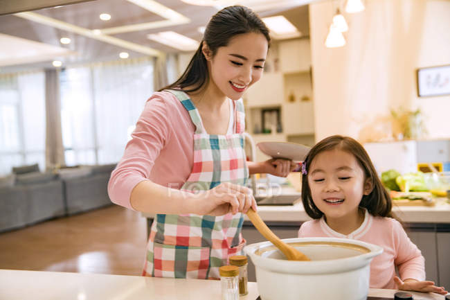 Happy asian mother and daughter cooking soup together in kitchen — Stock Photo