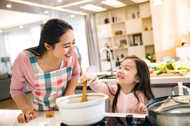 Happy asian mother and daughter cooking soup together in kitchen — Stock Photo
