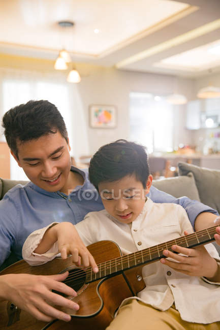 Счастливый китайский отец и сын играют вместе на акустической гитаре дома — стоковое фото