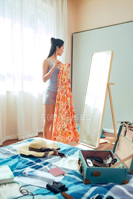 Vista lateral da bela menina asiática segurando vestido e olhando para o espelho — Fotografia de Stock