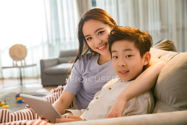 Щаслива мати з сином, використовуючи цифровий планшет і посміхаючись на камеру разом вдома — стокове фото