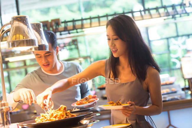 Feliz jovem asiático casal segurando pratos e escolher deliciosa comida em buffet — Fotografia de Stock