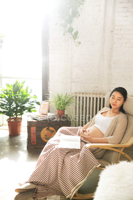 High angle view of young pregnant woman sleeping in chair with book — Stock Photo