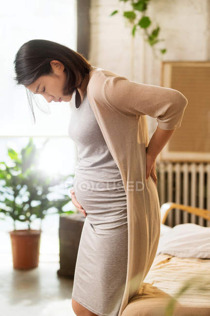 Vista lateral de la joven embarazada tocando el vientre y la espalda - foto de stock