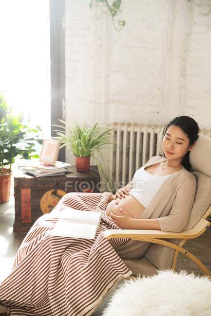 Молодая беременная женщина с закрытыми глазами сидит в кресле-качалке с закрытыми глазами — стоковое фото
