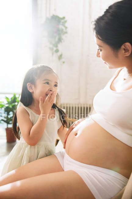 Adorável criança feliz tocando barriga de mãe jovem grávida em casa — Fotografia de Stock