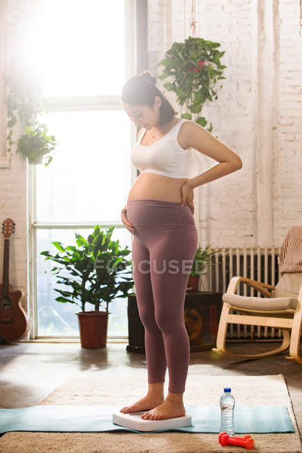 Sorrindo jovem grávida de pé em escalas e olhando para baixo em casa — Fotografia de Stock