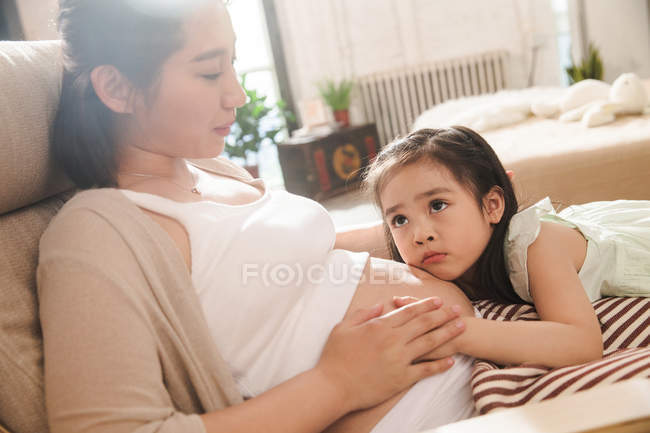 Маленький ребенок слушает животик беременной матери дома — стоковое фото