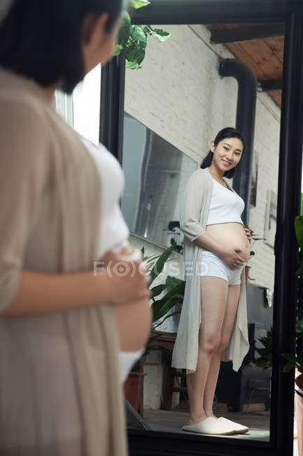 Messa a fuoco selettiva di felice giovane donna incinta guardando specchio a casa — Foto stock
