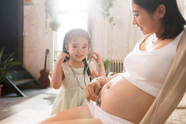 Entzückendes Kind mit Stethoskop spielt mit schwangerer Mutter — Stockfoto