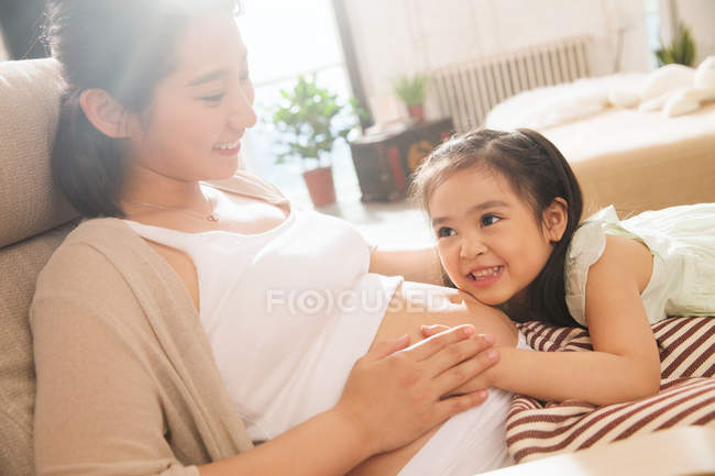 Adorabile sorridente bambino che abbraccia felice madre incinta a casa — Foto stock