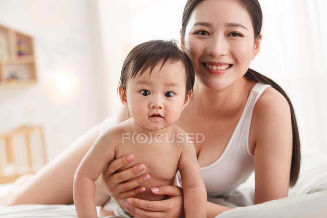 Счастливая молодая мама с восхитительным ребенком, вместе глядя в камеру — стоковое фото