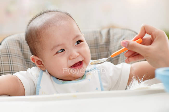 Tiro cortado de mãe segurando colher e alimentando bebê adorável — Fotografia de Stock