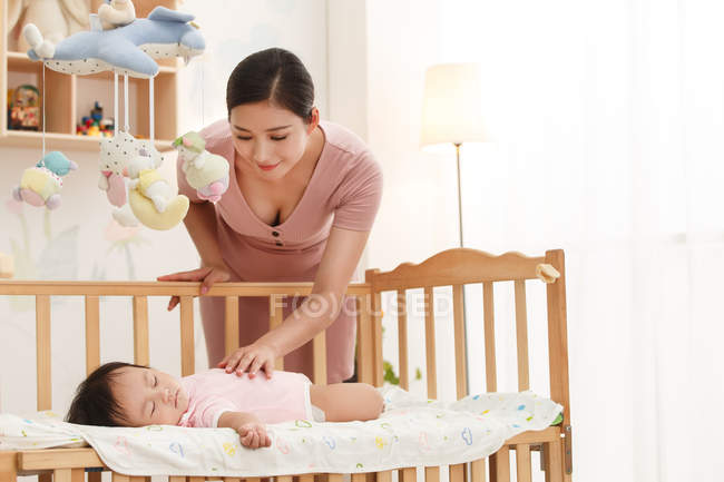 Smiling young mother looking at adorable infant baby lying in crib — Stock Photo