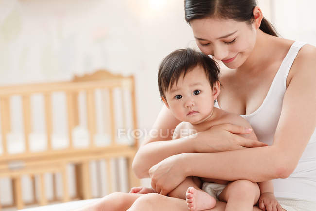 Счастливая молодая мама обнимает очаровательного ребенка глядя в камеру — стоковое фото