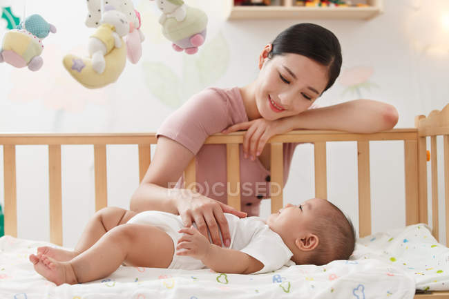 Lächelnde junge Mutter mit Blick auf entzückendes Baby, das im Kinderbett liegt — Stockfoto