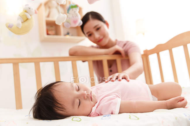Счастливая молодая мать смотрит на восхитительного младенца, спящего в кроватке — стоковое фото