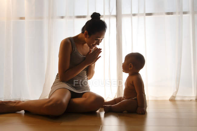 Happy young mother looking at adorable infant baby in diaper sitting on floor — Stock Photo