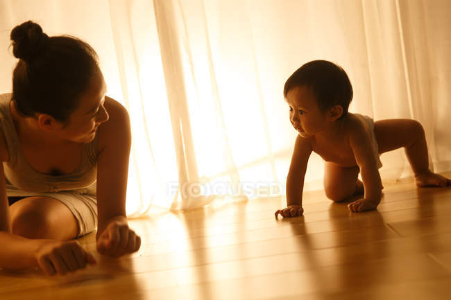 Feliz jovem mãe brincando com bebê adorável em fralda rastejando no chão — Fotografia de Stock