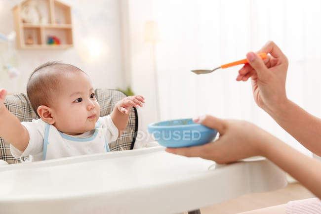 Recortado disparo de madre sosteniendo cuchara y alimentación adorable bebé - foto de stock