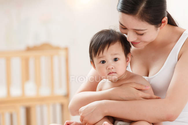 Sorrindo jovem mãe abraçando adorável bebê olhando para a câmera — Fotografia de Stock