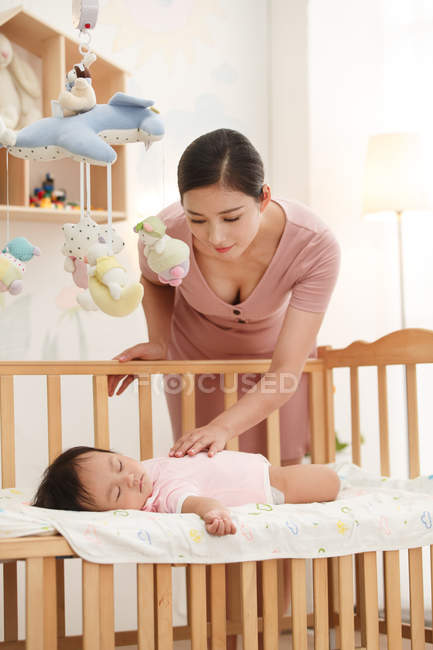 Junge Mutter schaut niedliches kleines Baby an, das im Kinderbett schläft — Stockfoto