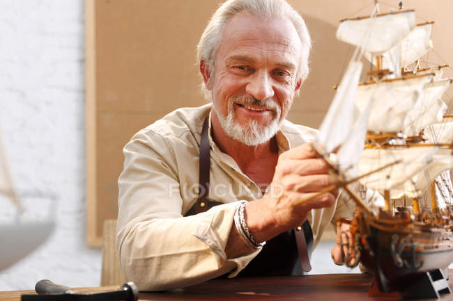 Sorridente uomo maturo facendo modello barca a vela in officina — Foto stock