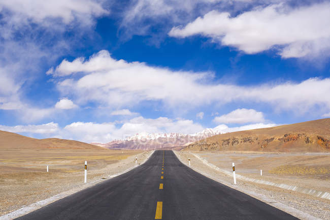 Strada asfaltata vuota tra colline panoramiche nella giornata di sole — Foto stock