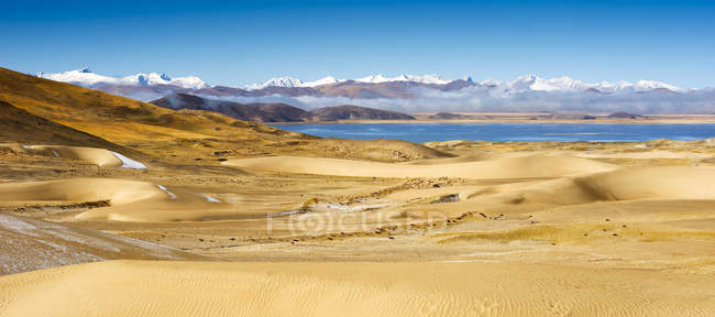 Удивительный пейзаж с песчаными дюнами, водоем и заснеженные горы на горизонте — стоковое фото