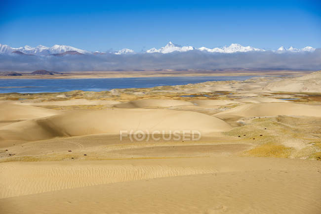 Dunas de areia, corpo de água e montanhas no horizonte no dia ensolarado — Fotografia de Stock