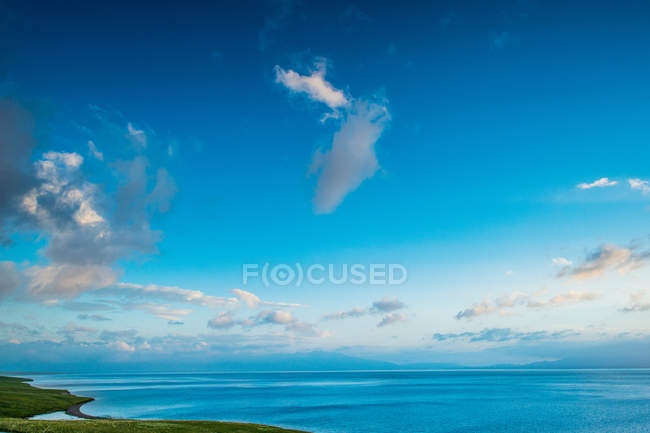 Costa verde e majestoso corpo de água sob o céu azul com nuvens no dia ensolarado — Fotografia de Stock