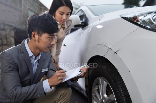 Jeune homme vérifiant les dommages de voiture avec la jeune femme — Photo de stock