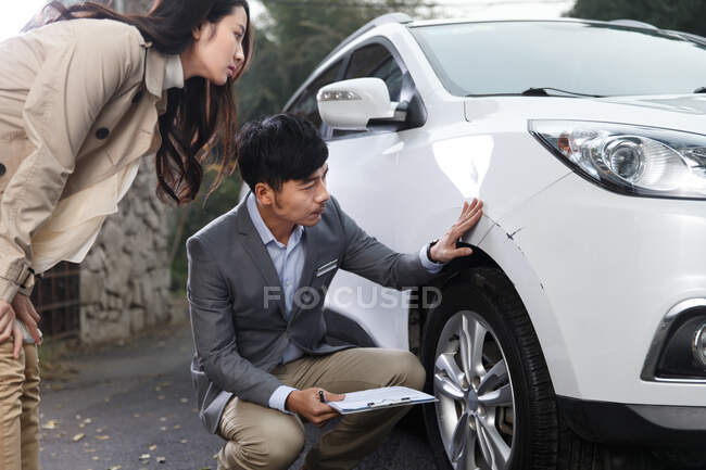 Молодий чоловік перевіряє пошкодження автомобіля з молодою жінкою — стокове фото