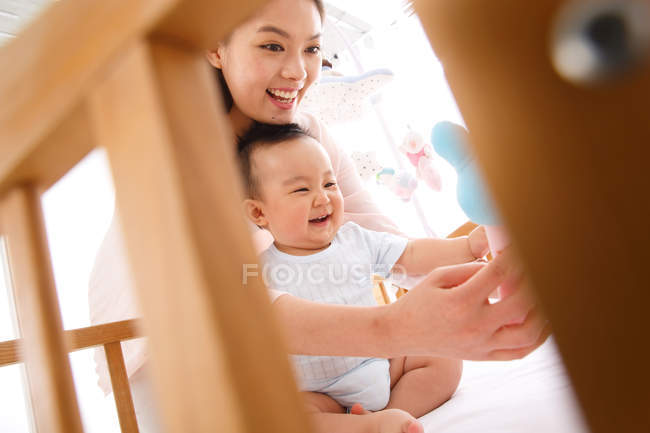 Feliz jovem mãe brincando com adorável bebê no berço, foco seletivo — Fotografia de Stock