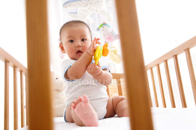 Selective focus of adorable asian baby boy sitting in crib and looking at camera — Stock Photo