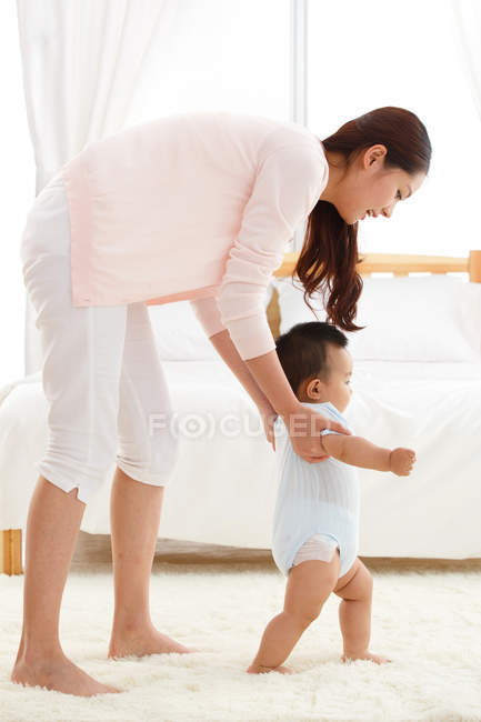 Young mother learning adorable little baby to walk at home — Stock Photo