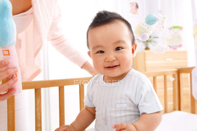 Adorable happy asian baby boy sitting in crib and looking at camera — Stock Photo