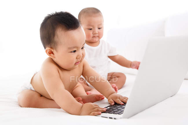 Cute babies using laptop computer on bed — Stock Photo