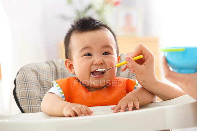 Tiro cortado de mãe segurando colher e alimentação adorável bebê pequeno — Fotografia de Stock