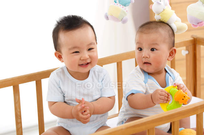 Two adorable happy chinese babies sitting together in crib — Stock Photo