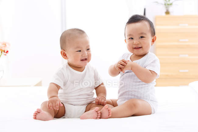 Two cute happy asian babies sitting together on bed — Stock Photo