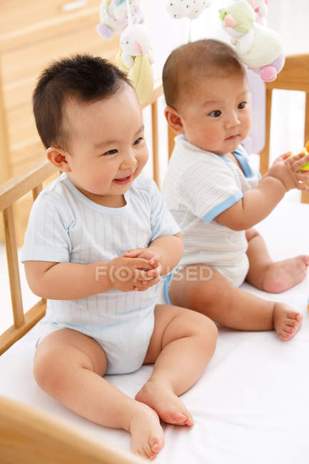 Two cute happy asian babies sitting together in crib — Stock Photo