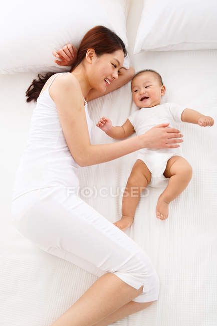 Высокий угол зрения счастливой молодой матери, смотрящей на восхитительного ребенка, спящего на кровати — стоковое фото