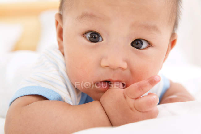 Close-up view of cute asian baby boy lying on bed and looking at camera — Stock Photo